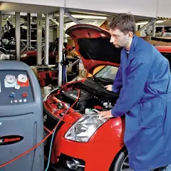 Mechanik przy czerwonym Suzuki wykonuje montaż klimatyzacji. Sprawdza cenę usługi i stan techniczny pojazdu.