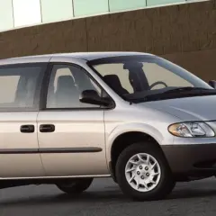 Srebrny Chrysler Voyager, gotowy na każdą podróż, zaparkowany przed budynkiem z ceglaną fasadą.