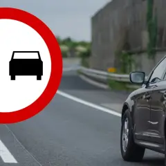 Znak zakazu wyprzedzania na podwójnej ciągłej. Czarny SUV jedzie po drodze, a na pierwszym planie znak drogowy.