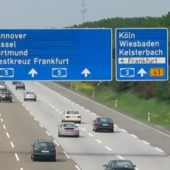 Niemiecki **autobahn** z niebieskimi tablicami kierunkowymi do Hanoweru, Kolonii i Monachium. Samochody jadą po wielopasmowej drodze.