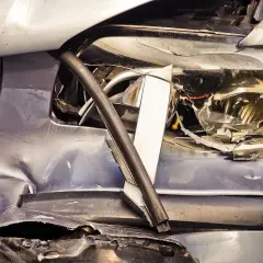 Zniszczony przód samochodu, pęknięty reflektor i wgniecenia. Pojazd po wypadku, czeka go wyrejestrowanie.