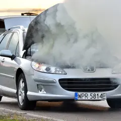 Srebrny Peugeot z otwartą maską i kłębami dymu. Chyba ten rozbiegany diesel potrzebuje mechanika.