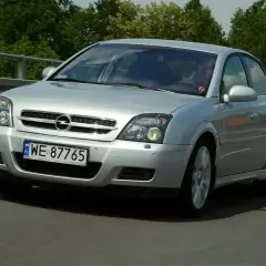 Srebrny Opel Vectra C GTS z polskimi tablicami WE 87765 jedzie po drodze, otoczony zielenią.