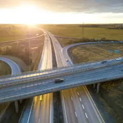 Widok z lotu ptaka na węzeł autostradowy o zachodzie słońca, z samochodami na jezdni.