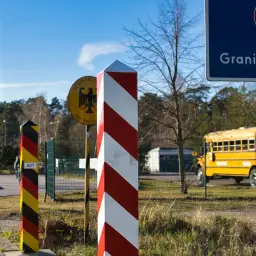 Słupki graniczne i znak "Granica Państwa" wskazują na kontrole na granicy niemieckiej. Żółty autobus szkolny czeka po stronie polskiej.