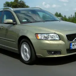 Złoty Volvo V50 na drodze, z zielonymi drzewami w tle.