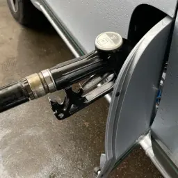 Pistolet do tankowania wlewa paliwo do samochodu. Krople deszczu na karoserii i mokry asfalt.