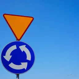Znak ustąp pierwszeństwa i znak ronda na tle błękitnego nieba.