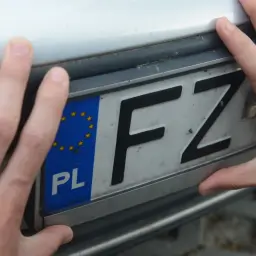 Dłonie trzymają tablice rejestracyjne województwa z symbolem Unii Europejskiej i literami FZ.