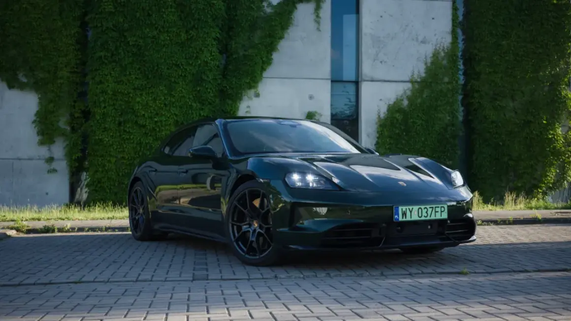 Ciemnozielony Porsche Taycan na tle nowoczesnego budynku z pnączami.