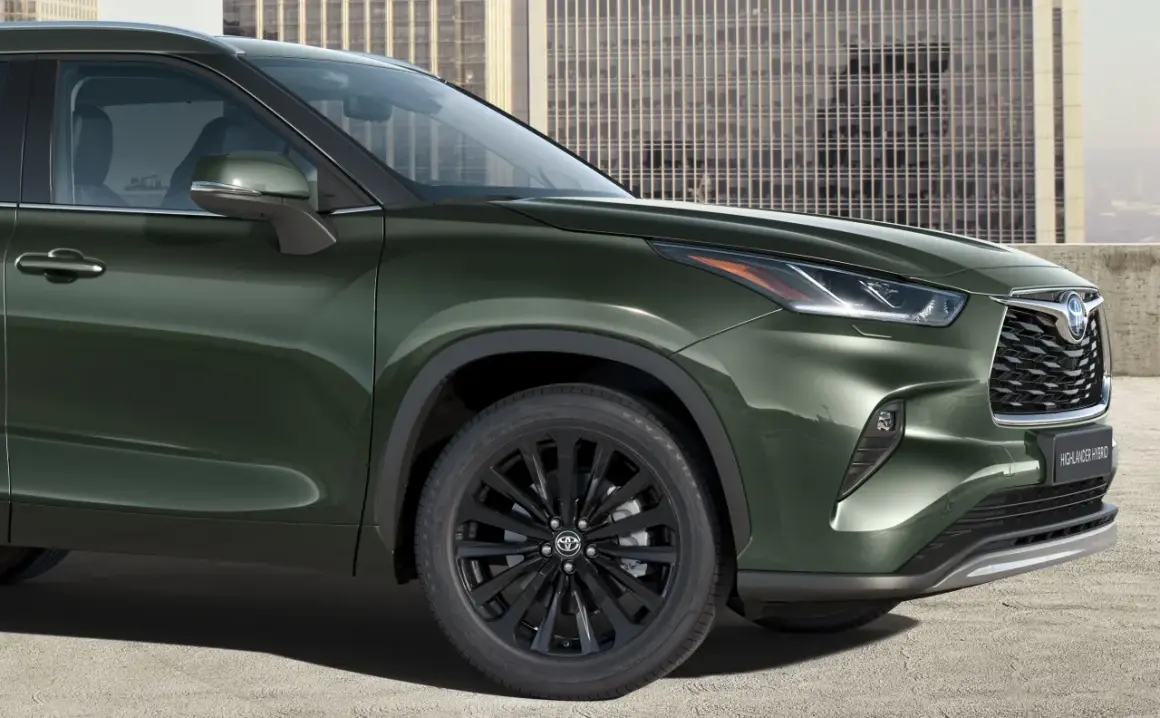 Zielony Toyota Highlander z czarnymi felgami stoi przed nowoczesnym budynkiem.