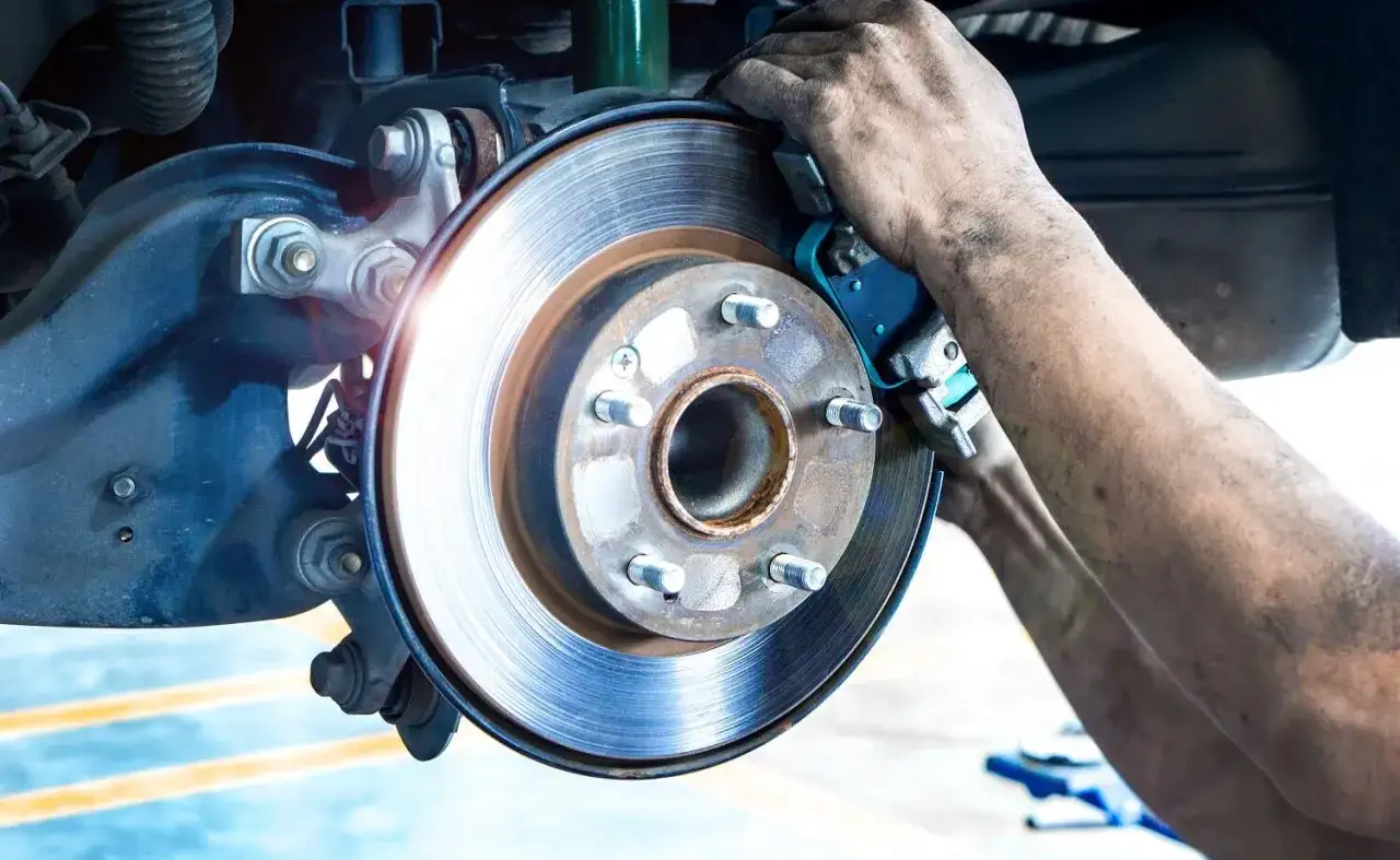 Mechanik pracuje nad tarczą hamulcową, dbając o sprawny układ hamulcowy pojazdu.