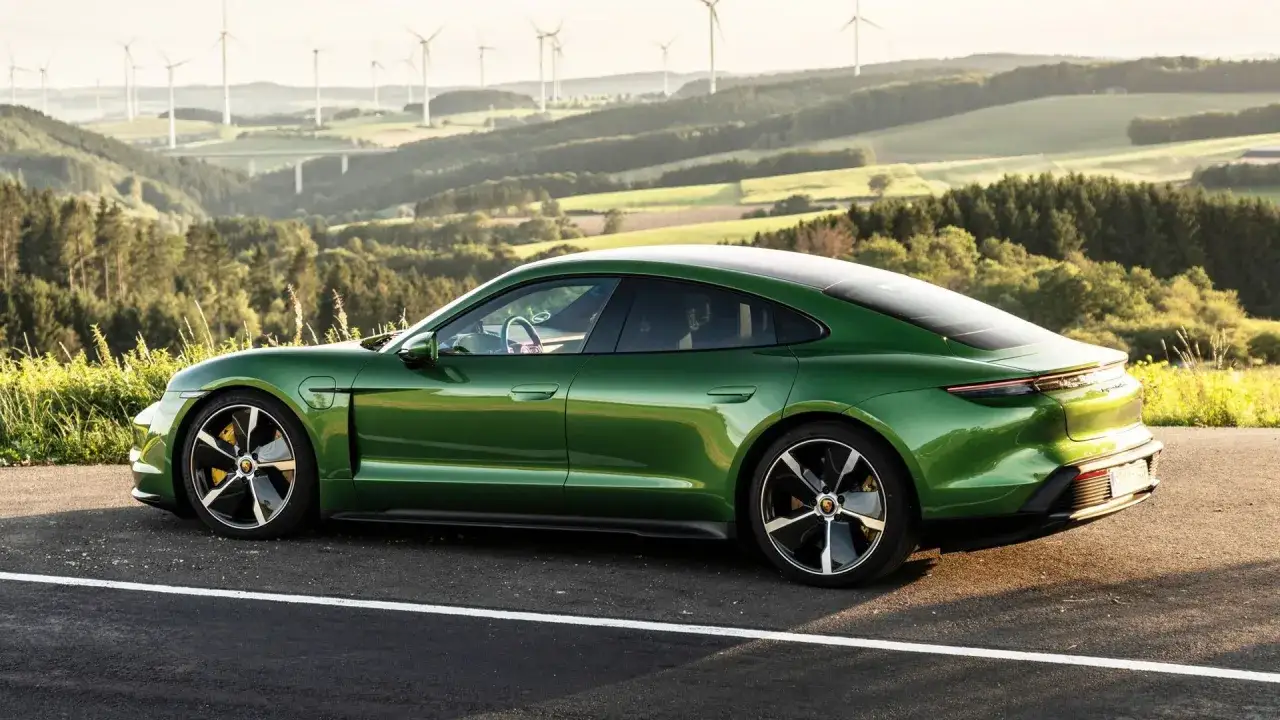 Zielony Porsche Taycan na tle krajobrazu z wiatrakami.