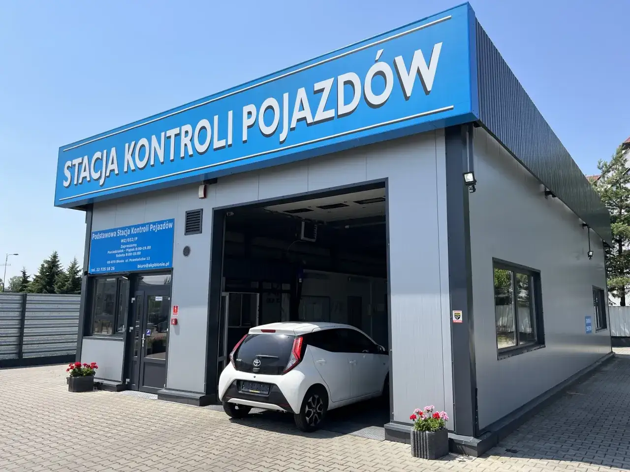 Stacja kontroli pojazdów, gdzie dowiesz się, ile kosztuje przegląd samochodu. Biały Toyota Aygo wjeżdża do środka.