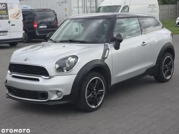 Srebrny mini paceman z czarnym dachem i felgami, zaparkowany na placu.