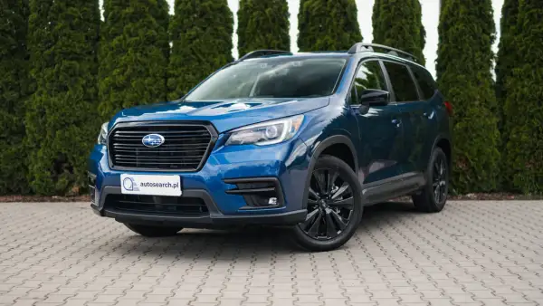 Błękitny Subaru Ascent z czarnymi felgami stoi przed żywopłotem.