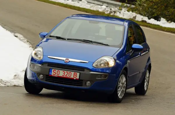 Niebieski Fiat Punto jedzie po drodze, na której widać śnieg. Z przodu widoczne są **czerwone tablice rejestracyjne** z numerem SO 320 B.