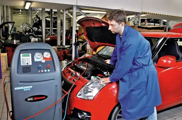 Mechanik przy czerwonym Suzuki wykonuje montaż klimatyzacji. Sprawdza cenę usługi i stan techniczny pojazdu.