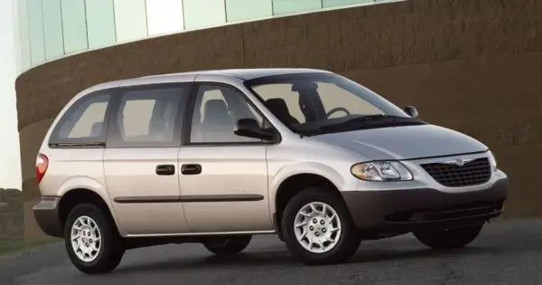 Srebrny Chrysler Voyager, gotowy na każdą podróż, zaparkowany przed budynkiem z ceglaną fasadą.