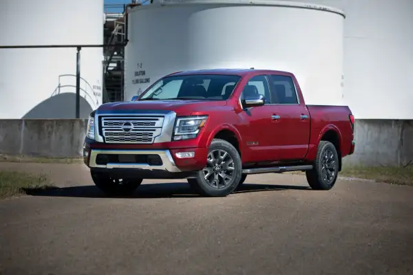 Czerwony Nissan Titan z chromowanymi detalami stoi na asfalcie przed białymi zbiornikami przemysłowymi.