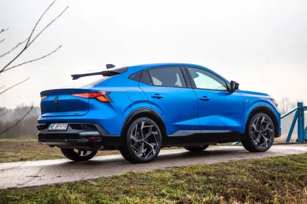 Niebieski Renault Rafale z dynamiczną linią dachu, zaparkowany na mokrej drodze.