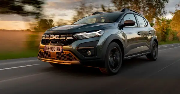 Zielony Dacia Sandero Stepway pędzi po drodze o zachodzie słońca, otoczony rozmazanymi drzewami i mglistym krajobrazem.