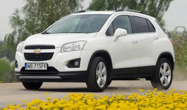 Biały Chevrolet Trax jedzie po drodze, otoczony żółtymi kwiatami.