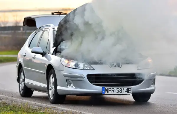 Srebrny Peugeot z otwartą maską i kłębami dymu. Chyba ten rozbiegany diesel potrzebuje mechanika.
