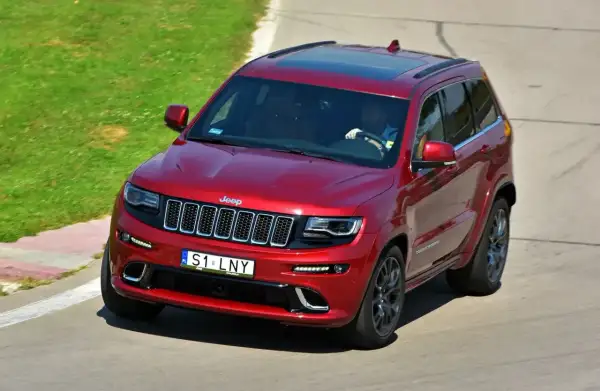 Czerwony Jeep Grand Cherokee z indywidualnymi tablicami rejestracyjnymi "S1 LNY" na torze wyścigowym.
