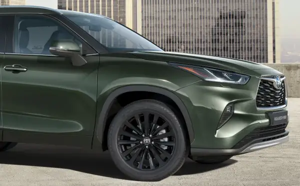 Zielony Toyota Highlander z czarnymi felgami stoi przed nowoczesnym budynkiem.