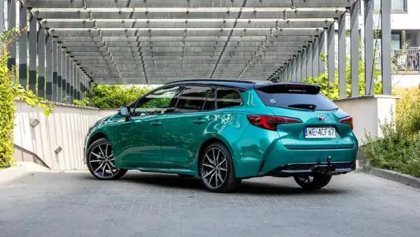 Zielona Toyota Corolla Hybrid kombi z czarnym dachem, zaparkowana pod nowoczesną pergolą.